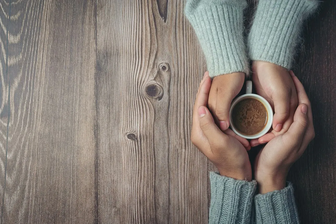Two people holding a warm cup of coffee together